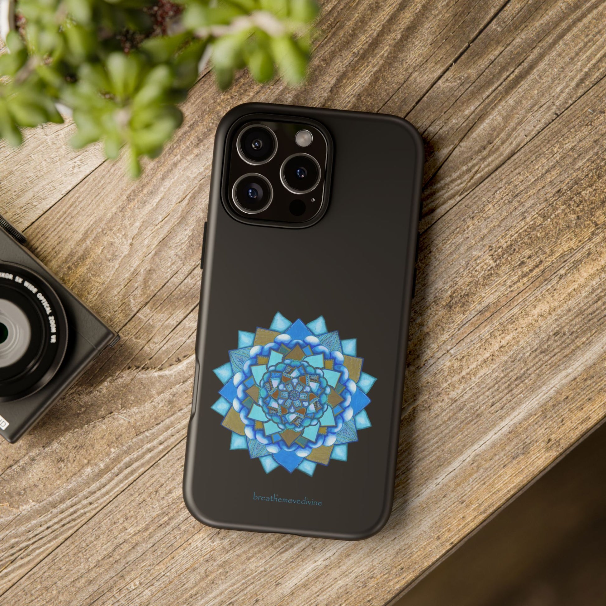 Phone case with blue geometric design on a wooden surface next to a camera and plant.